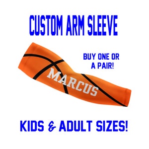 May include: Orange and black basketball arm sleeve with the name "MARCUS" printed in white.  "CUSTOM ARM SLEEVE" and "BUY ONE OR A PAIR!" are printed in blue.  "KIDS & ADULT SIZES!" is printed in blue at the bottom.