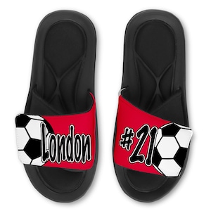 May include: Black slide sandals with a red and white soccer ball design. The strap has the name "London" and the number "#21" printed on it.