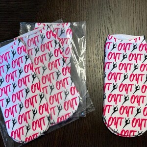 May include: Three pairs of white socks with a pink and black repeating pattern of the word "OUT" and a stylized dancer figure.