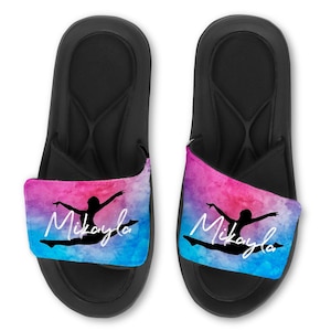 May include: A pair of black slides with a pink and blue watercolor design featuring a silhouette of a gymnast and the name "Mikayla".