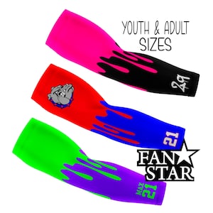 May include: Three colorful arm sleeves with a dripping paint design. The sleeves are in pink, red, and green with black, blue, and purple paint dripping down. The sleeves have numbers 29 and 21 printed on them. The sleeves are labeled "FAN STAR" and "MAX".