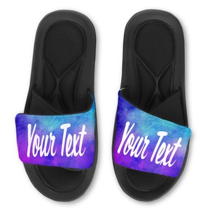 May include: A pair of black slide sandals with a blue and purple watercolor design on the strap. The strap has the text "Your Text" in white.