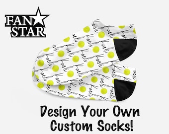 May include: A pair of white ankle socks with a black heel and toe. The socks feature a repeating pattern of yellow circles and the word "kaeli" written in black.