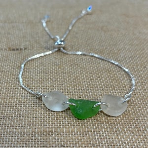 Puede incluir: Un brazalete de cadena plateada con una pieza de vidrio de mar verde y dos blancas. El brazalete tiene un cierre deslizante.