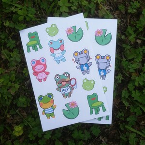 May include: Sheets of stickers featuring cartoon frogs in various outfits and poses. Some frogs are wearing dresses, robot suits, and striped shirts. Other stickers include lily pads, chairs, and frog faces.