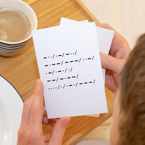 May include: A white card with black dashes and slashes written on it. The card is being held by a person's hand.