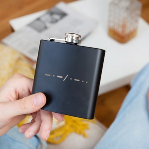 May include: A black metal flask with a silver top and a series of dashes and a slash on the front.