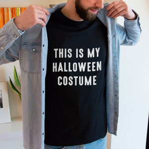 May include: A black t-shirt with white text that reads "This is my Halloween costume". The shirt is being worn by a person wearing a light blue denim shirt.