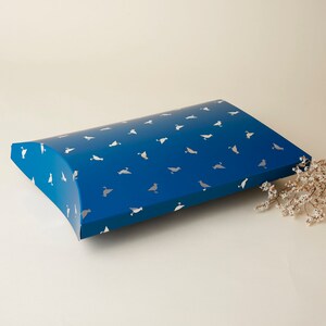 May include: A blue pillow box with a white bird pattern. The box is made of cardboard and has a curved shape.