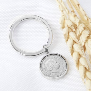 May include: Silver keyring featuring a 2002 British one pound coin with a profile of Queen Elizabeth II. The coin is attached to a silver ring.