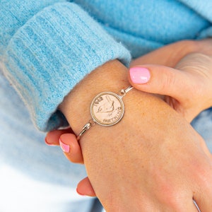 May include: A silver bracelet with a 1942 Farthing coin charm featuring a bird. The coin is copper coloured and has a raised design.