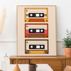 May include: A framed print with a retro design featuring three vintage cassette tapes in orange, brown, and pink colors on a beige background.