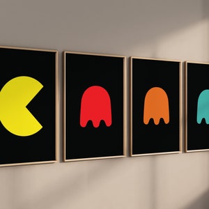 K&ouml;nnte beinhalten: Vier gerahmte Kunstdrucke mit Pac-Man und Geisterfiguren. Der erste Druck zeigt eine gelbe Pac-Man-Form. Die anderen drei Drucke zeigen rote, orangefarbene und t&uuml;rkisfarbene Geisterformen auf schwarzem Hintergrund. Jeder Druck ist in einem goldenen Rahmen.