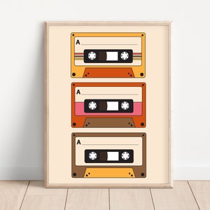 May include: A framed print with three vintage cassette tapes in a retro style. The tapes are stacked vertically and have a yellow, orange, and brown color scheme. The tapes have the letter "A" printed on them.