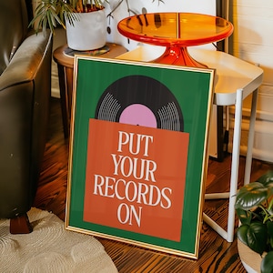 May include: Framed art print featuring a vinyl record design. The artwork has a green background with an orange record sleeve and a black record with a pink center. The text "PUT YOUR RECORDS ON" is displayed on the sleeve.