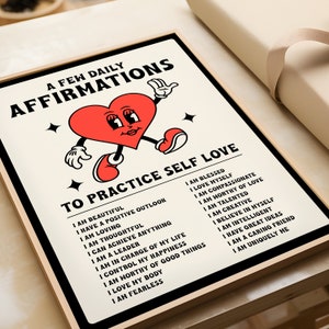 May include: A framed print with the words "A Few Daily Affirmations" and "To Practice Self Love." The print features a cartoon heart character with arms and legs. The affirmations are listed in black text on a cream background.
