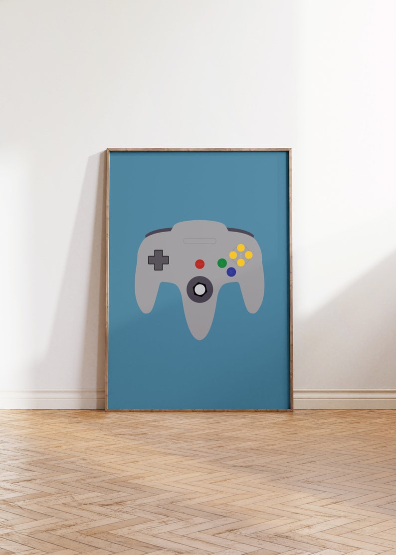 May include: A framed poster with a blue background and a gray Nintendo 64 controller in the center. The controller has a red button, green button, and yellow buttons.