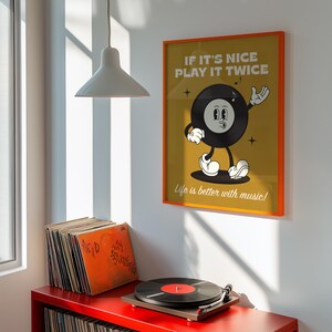 Puede incluir: Un p&oacute;ster enmarcado con borde naranja muestra un personaje de disco de vinilo de dibujos animados con el texto "If it's nice play it twice" y "Life is better with music!". Un tocadiscos y pilas de discos de vinilo est&aacute;n en un estante rojo.