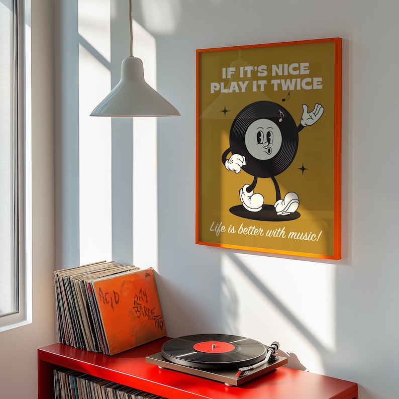 Puede incluir: Un p&oacute;ster enmarcado con borde naranja muestra un personaje de disco de vinilo de dibujos animados con el texto "If it's nice play it twice" y "Life is better with music!". Un tocadiscos y pilas de discos de vinilo est&aacute;n en un estante rojo.