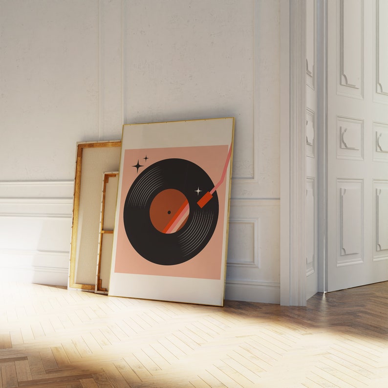 May include: A framed print of a black vinyl record with a pink background. The record has a red and orange stripe on the label. The print has a gold frame.