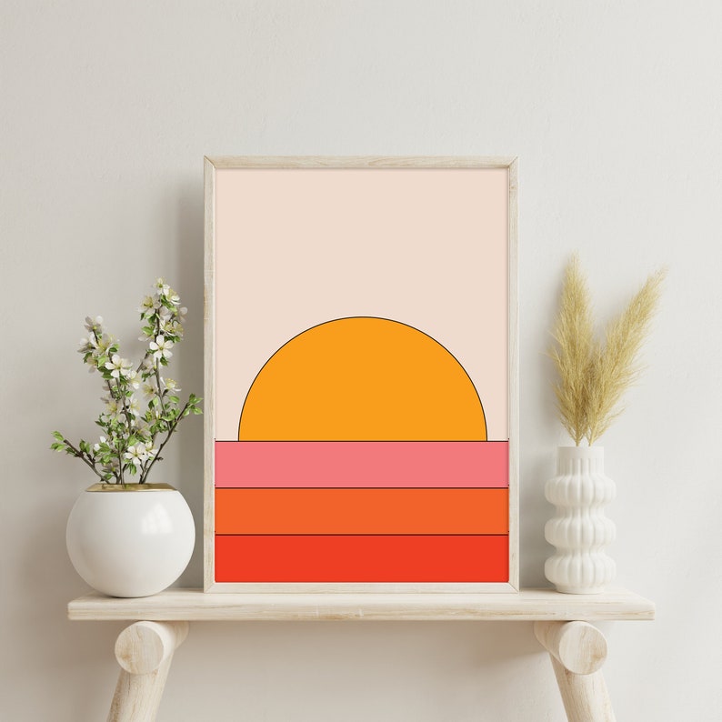 May include: A framed print of a sunset with a half-circle orange sun over a series of horizontal stripes in pink, orange, and red.