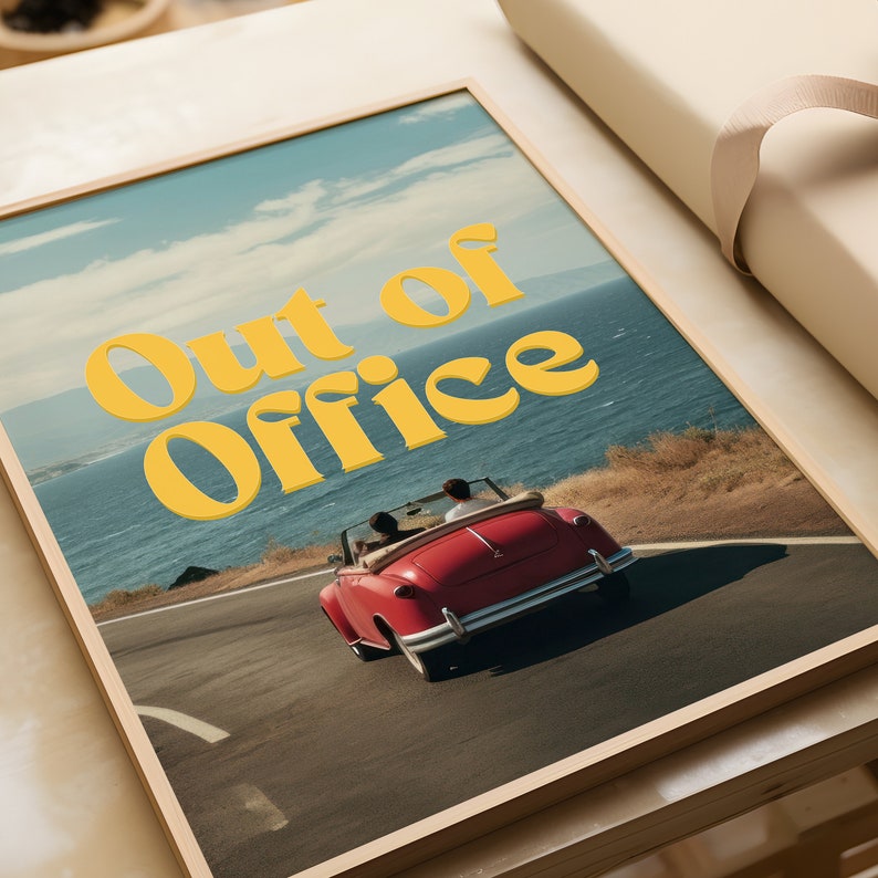May include: A framed print with a vintage aesthetic featuring a red convertible car driving along a coastal road with the text "Out of Office" in yellow letters.