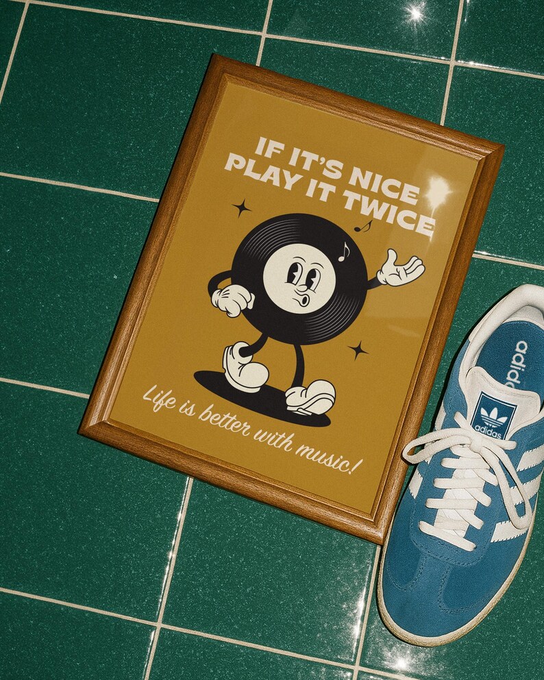 Puede incluir: Un estampado enmarcado con un personaje de disco de vinilo de dibujos animados sobre un fondo amarillo mostaza. El texto dice "IF IT'S NICE PLAY IT TWICE" y "Life is better with music!". Una zapatilla azul y blanca est&aacute; al lado.