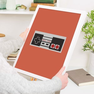 May include: A framed print of a retro video game controller with red buttons and the words "Select" and "Start" on a red background.