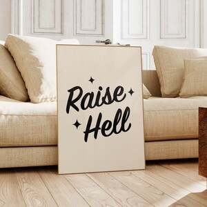 May include: A beige poster with black text that reads "Raise Hell" with two small stars on either side of the text. The poster is leaning against a beige couch.