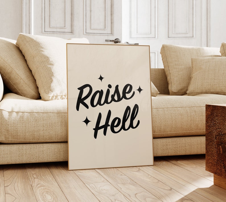 May include: A beige poster with black text that reads "Raise Hell" with two small stars on either side of the text. The poster is leaning against a beige couch.