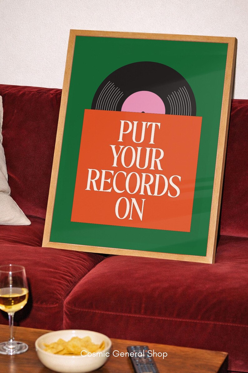 May include: A framed art print with a green background and a black vinyl record graphic. The print features the text "PUT YOUR RECORDS ON" in white on an orange background. The frame is a light wood color.