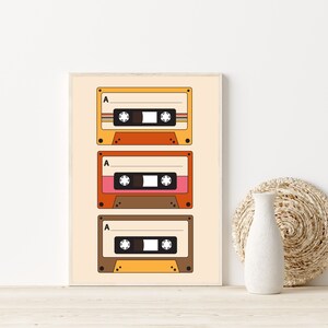 May include: A framed print of three vintage cassette tapes with the letter "A" on each tape. The tapes are stacked vertically and have a retro color scheme of orange, yellow, and brown.