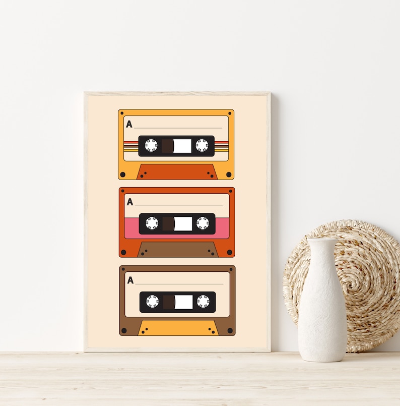 May include: A framed print of three vintage cassette tapes with the letter "A" on each tape. The tapes are stacked vertically and have a retro color scheme of orange, yellow, and brown.
