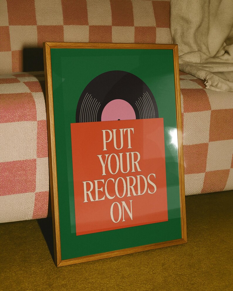 May include: A framed art print featuring a vinyl record design. The artwork has a green background with a black record and pink center. The text "PUT YOUR RECORDS ON" is displayed on a red rectangle. The frame is made of wood.