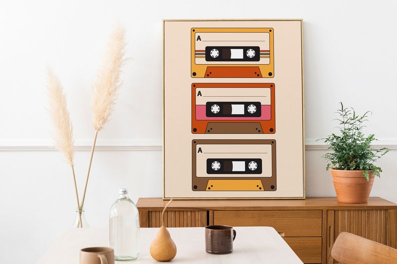 May include: A framed print with a retro design featuring three vintage cassette tapes in orange, brown, and pink colors on a beige background.