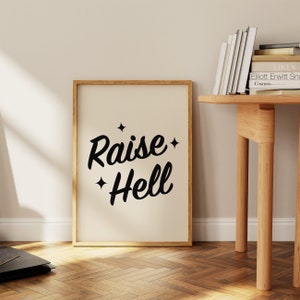 May include: A framed print with a white background and black text that reads "Raise Hell" with two small stars on either side of the text.