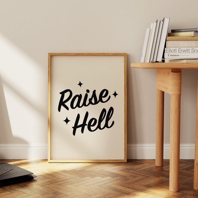 May include: A framed print with a white background and black text that reads "Raise Hell" with two small stars on either side of the text.