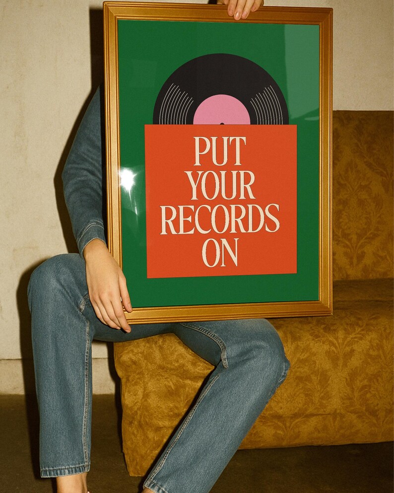 May include: A framed art print featuring a vinyl record design. The artwork has a green background with a black and pink record and an orange square with the text "PUT YOUR RECORDS ON" in white. The frame is gold.