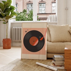 May include: A framed print of a black vinyl record with a red and orange design on a pink background. The record is surrounded by white stars. The print is hanging on a wall in a living room.