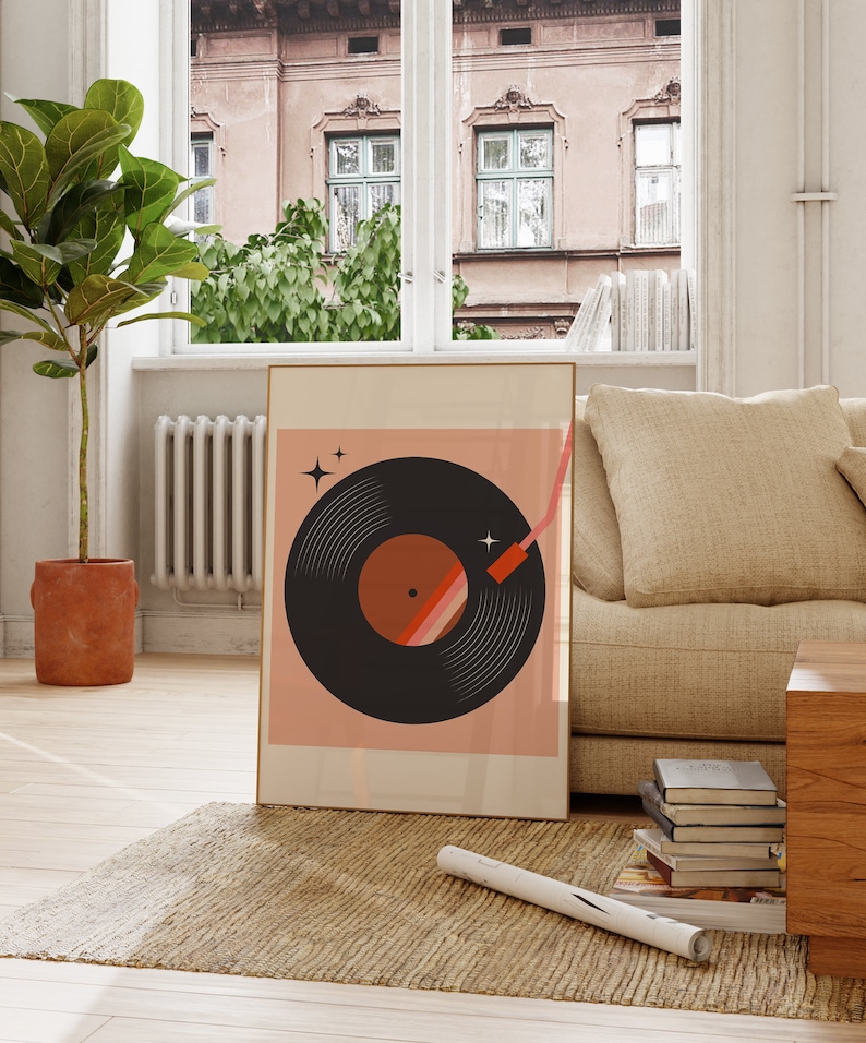 May include: A framed print of a black vinyl record with a red and orange design on a pink background. The record is surrounded by white stars. The print is hanging on a wall in a living room.