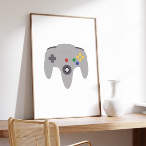 Puede incluir: Una impresi&oacute;n enmarcada de un mando de Nintendo 64 gris con botones de colores sobre un fondo blanco.