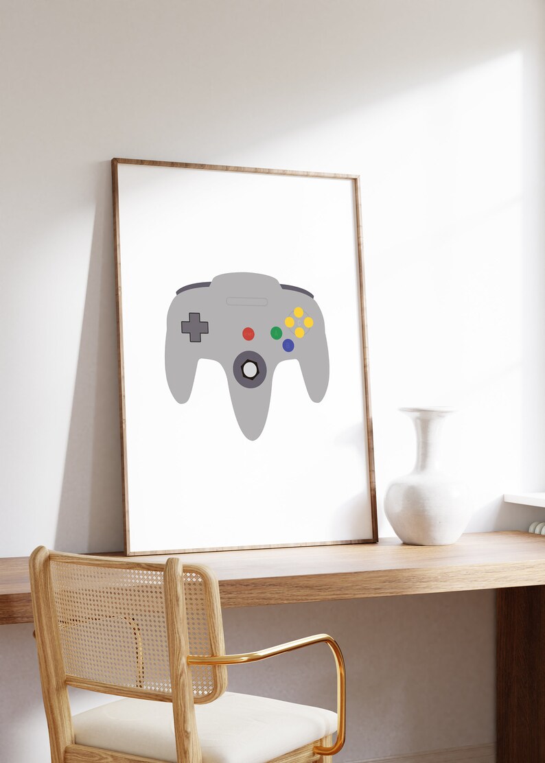 Puede incluir: Una impresi&oacute;n enmarcada de un mando de Nintendo 64 gris con botones de colores sobre un fondo blanco.