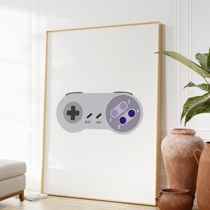 Puede incluir: Una impresi&oacute;n enmarcada de un mando de Super Nintendo gris y morado con las palabras "Select", "Start", "Y", "B", "X" y "A" impresas en &eacute;l.