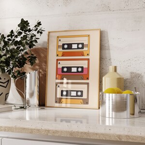 May include: A framed print of three vintage cassette tapes with the letter "A" and a number on each tape. The tapes are yellow, orange, and pink.