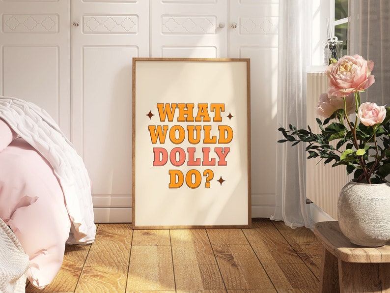 K&ouml;nnte beinhalten: Ein gerahmter Druck mit wei&szlig;em Hintergrund und dem Text "WHAT WOULD DOLLY DO?" in orangefarbenen und rosafarbenen Buchstaben mit einem Stern auf jeder Seite des Textes.