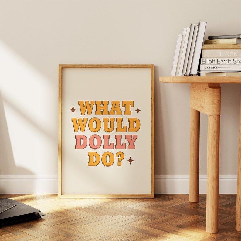 K&ouml;nnte beinhalten: Ein gerahmter Druck mit wei&szlig;em Hintergrund und dem Text "WHAT WOULD DOLLY DO?" in gelben, orangefarbenen und rosafarbenen Buchstaben. Die Buchstaben sind schwarz umrandet und haben einen Retro-Stil.