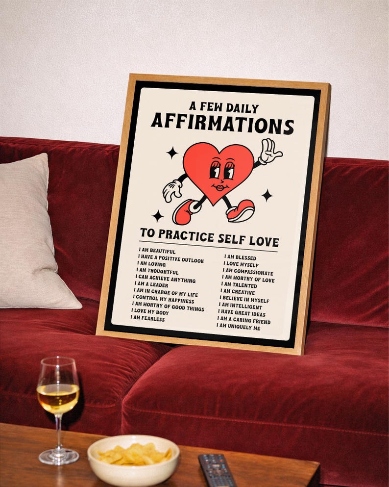 May include: A framed print with the text "A Few Daily Affirmations" and "To Practice Self Love." The artwork features a cartoon heart with arms and legs. The print is displayed on a red velvet couch.
