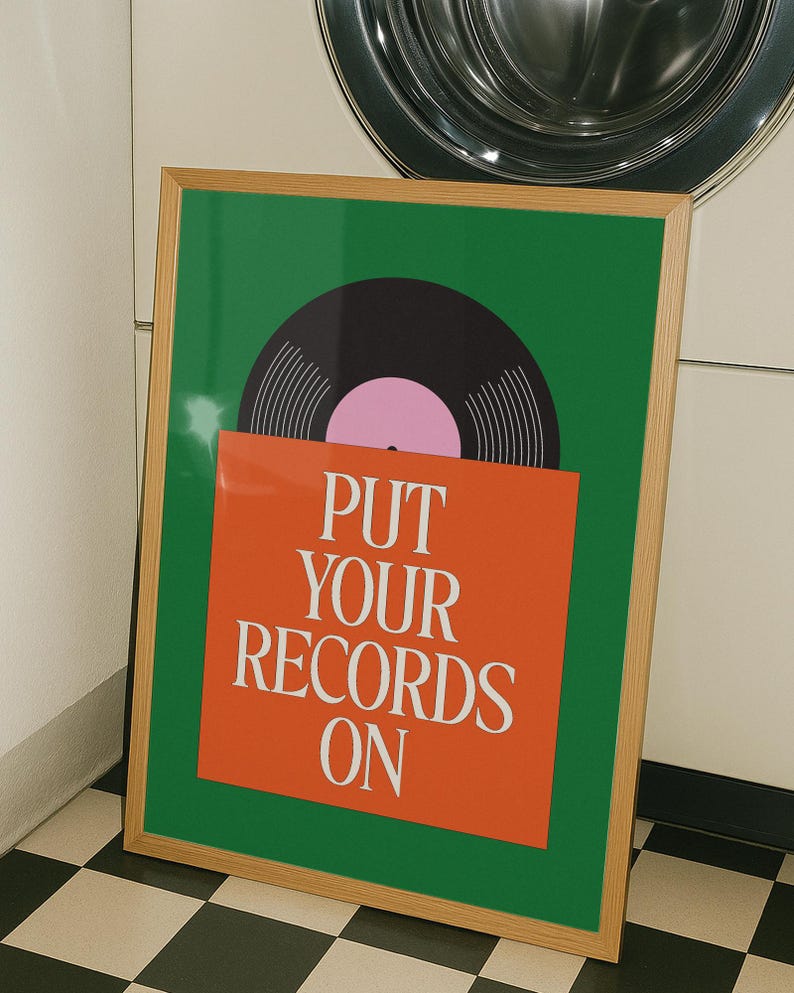 May include: A framed poster with a green background and a vinyl record graphic. The record is black with a pink center. An orange rectangle at the bottom has the text "PUT YOUR RECORDS ON" in white.