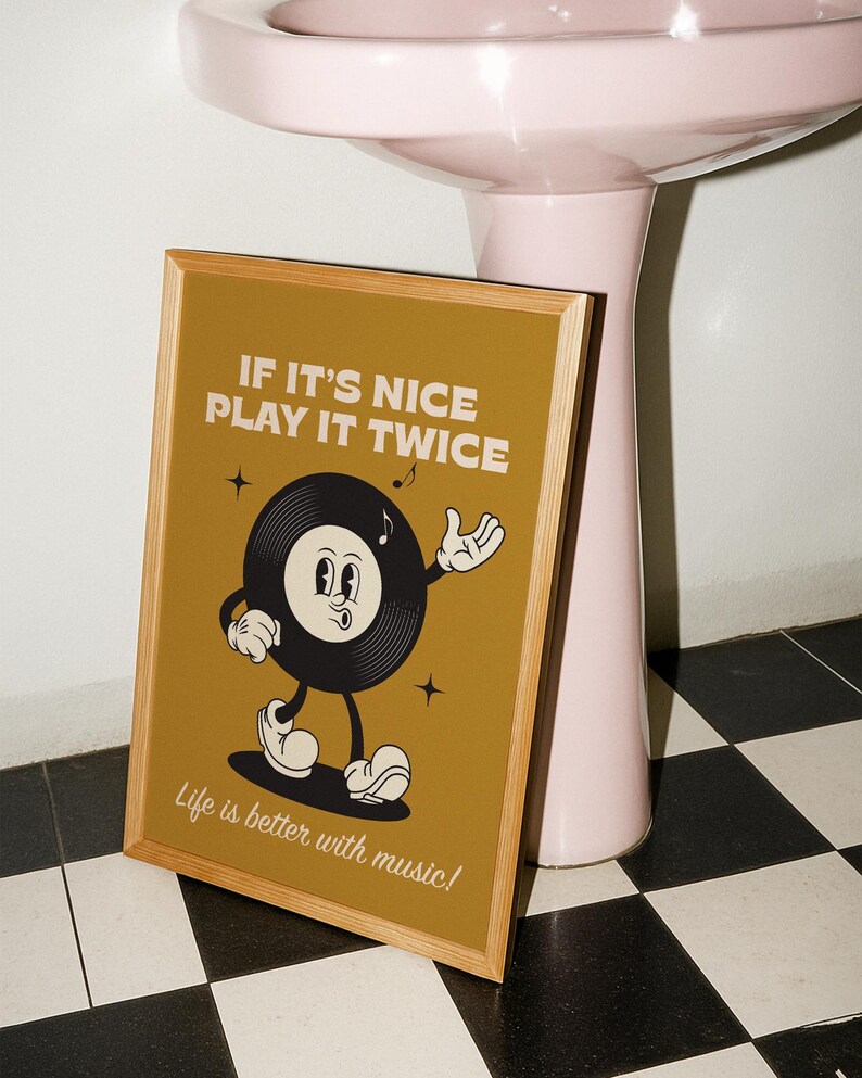 Puede incluir: Un p&oacute;ster enmarcado con un personaje de disco de vinilo de dibujos animados sobre un fondo amarillo mostaza. El texto dice "IF IT'S NICE PLAY IT TWICE" y "Life is better with music!". El marco es de color marr&oacute;n claro.