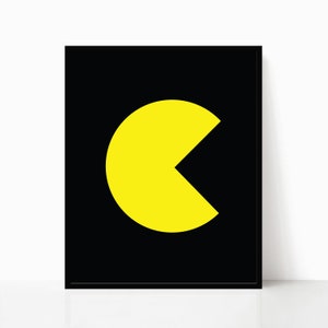 K&ouml;nnte beinhalten: Gerahmter Druck mit einer gelben Pac-Man-Figur auf schwarzem Hintergrund. Das Kunstwerk ist minimalistisch gestaltet, mit der Form der ikonischen Videospiel-Figur. Der Druck ist vor einer wei&szlig;en Wand platziert.